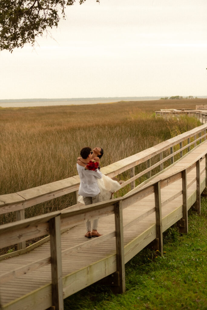 Bride and groom embracing at candlelight elopement in Wilmington North Carolina captured by A Visual Anthropologist”

“Couple running together through grass field at North Carolina coastal elopement”