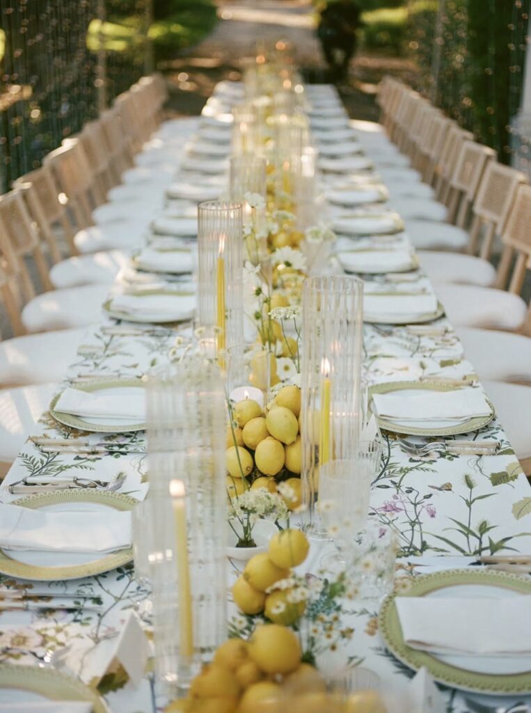 Alfresco wedding table with lemon centerpieces and candlelight designed by Laurel and Fey at Lloyd Butler Ranch.”
“Close-up of lemon-themed wedding tablescape with floral linens and crystal glassware.”