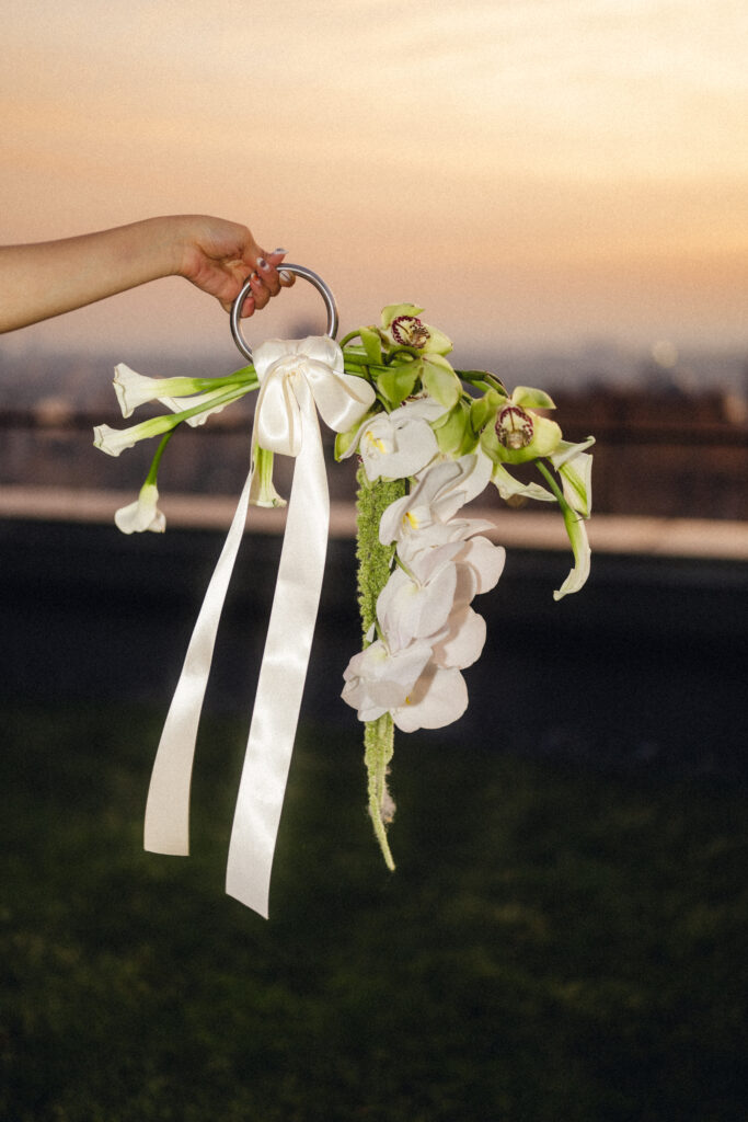 Contemporary white orchid wedding bouquet with ribbon on a rooftop overlooking New York City at sunset
