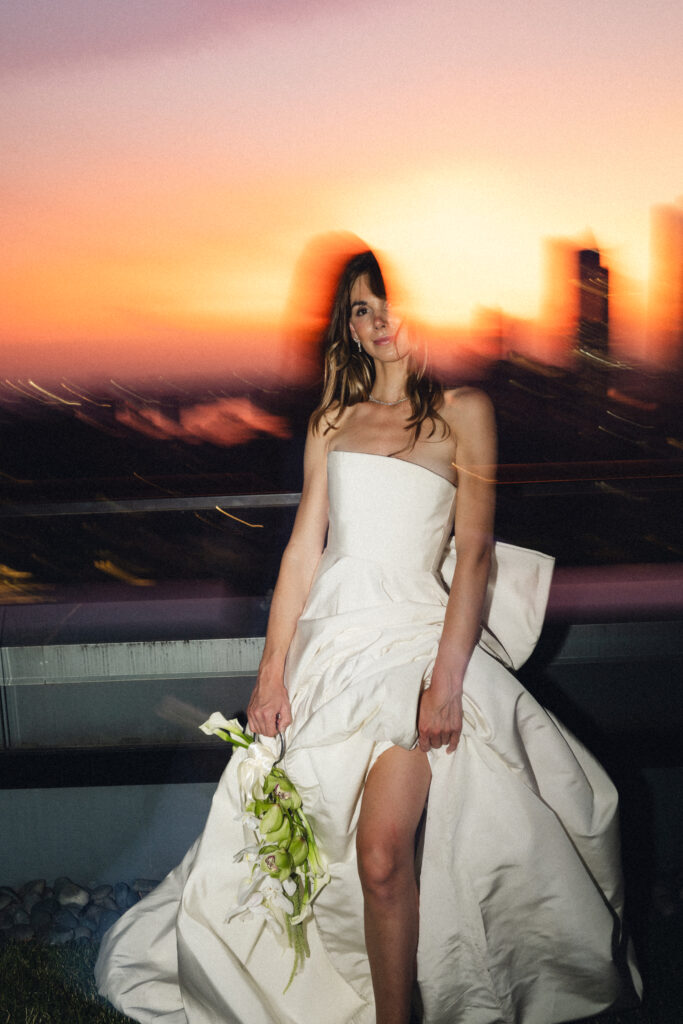New York bride in a strapless gown holding a sculptural orchid bouquet with sunset motion-blur effect on a Manhattan rooftop.

Editorial rooftop bridal portrait in New York City during golden hour with blurred skyline in the background.
