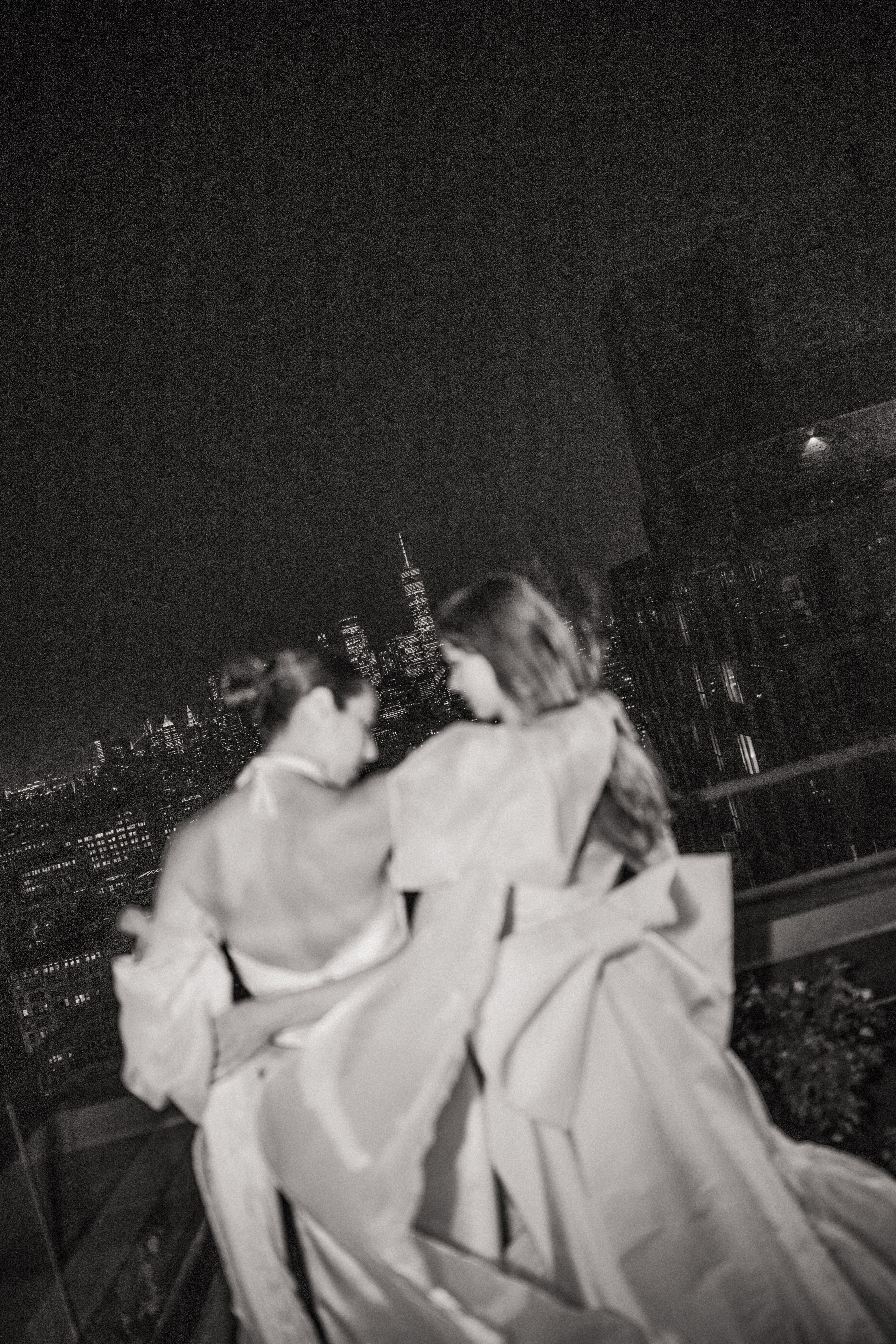 Black-and-white nighttime rooftop portrait of two brides with the New York City skyline in the background.