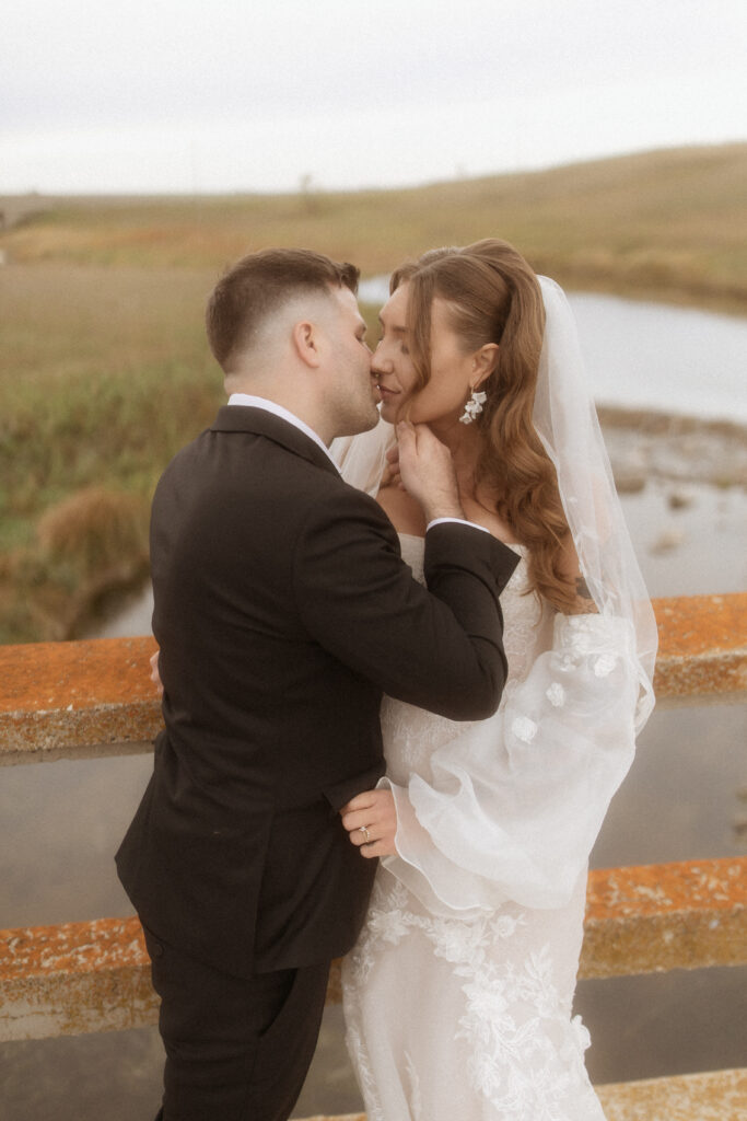 Couple kissing under bridal veil in soft light by Saskatchewan wedding photographer VAIS Images”