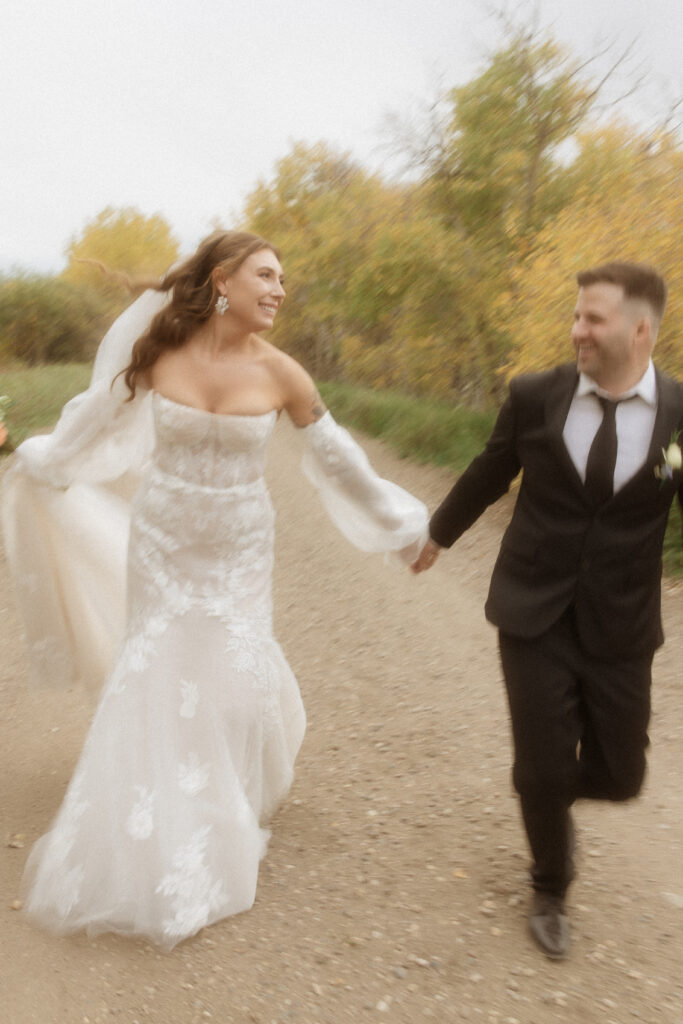Bride walking down Saskatchewan country road in lace off-the-shoulder wedding gown photographed by VAIS Images