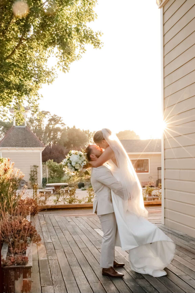 Groom lifting bride on the wooden deck at Garden Valley Ranch as the sun sets behind them.