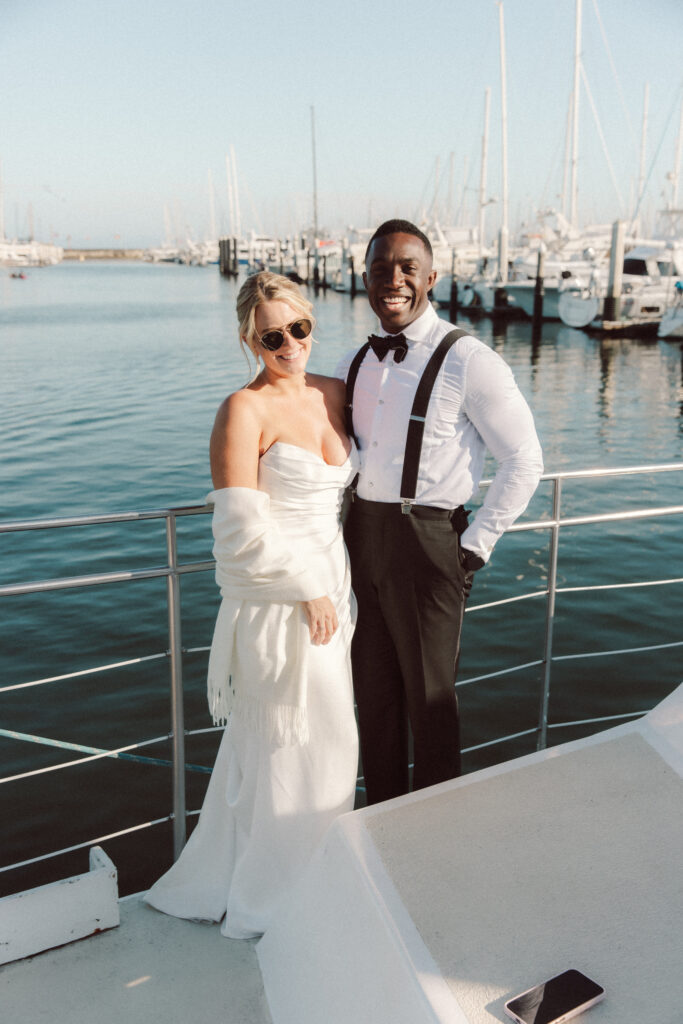 Couple posing by the marina in Santa Barbara after a wedding adventure day, with sailboats in the background and coastal light.