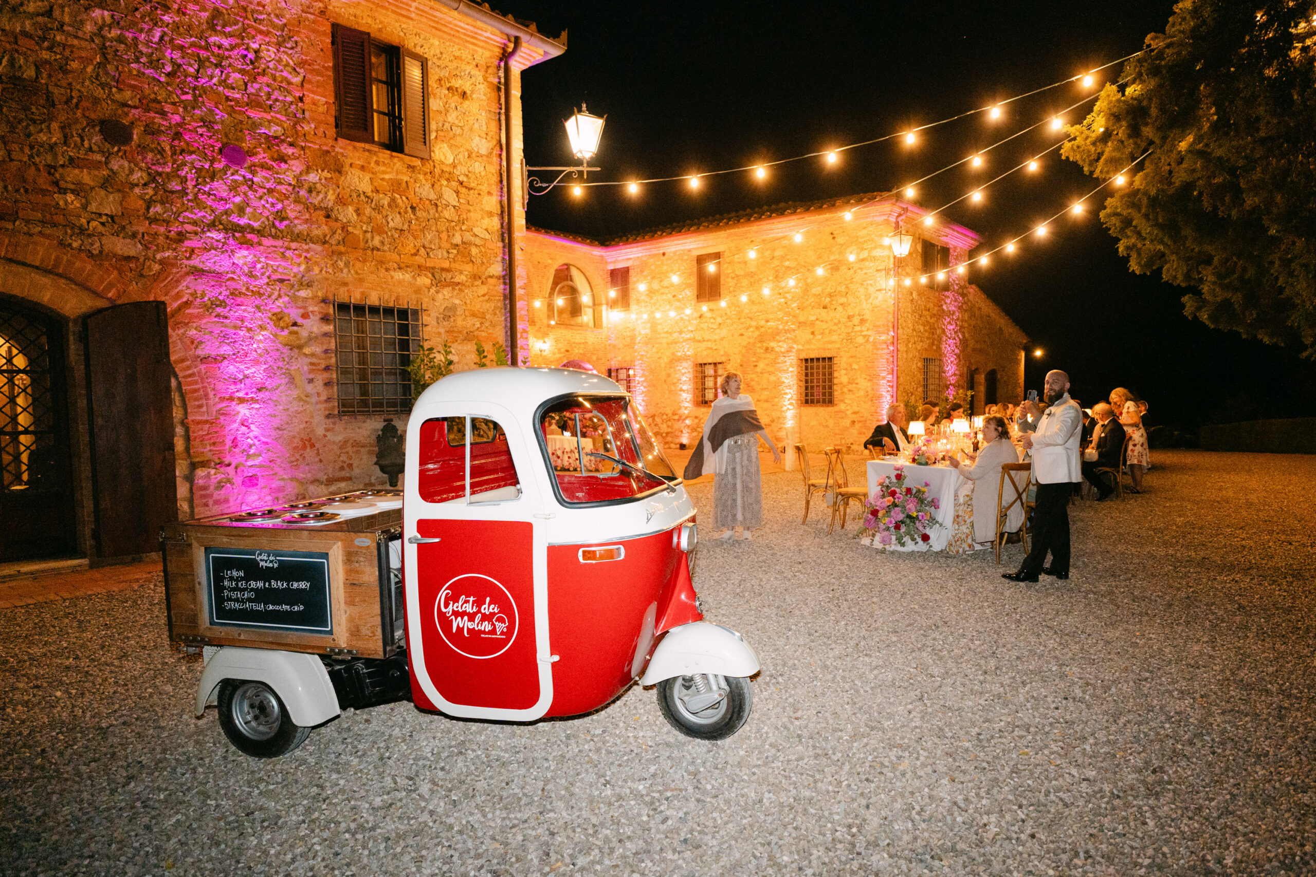 Night pizza party with string lights and a vintage red Ape cart in the courtyard of Villa Boscarello, Tuscany destination wedding