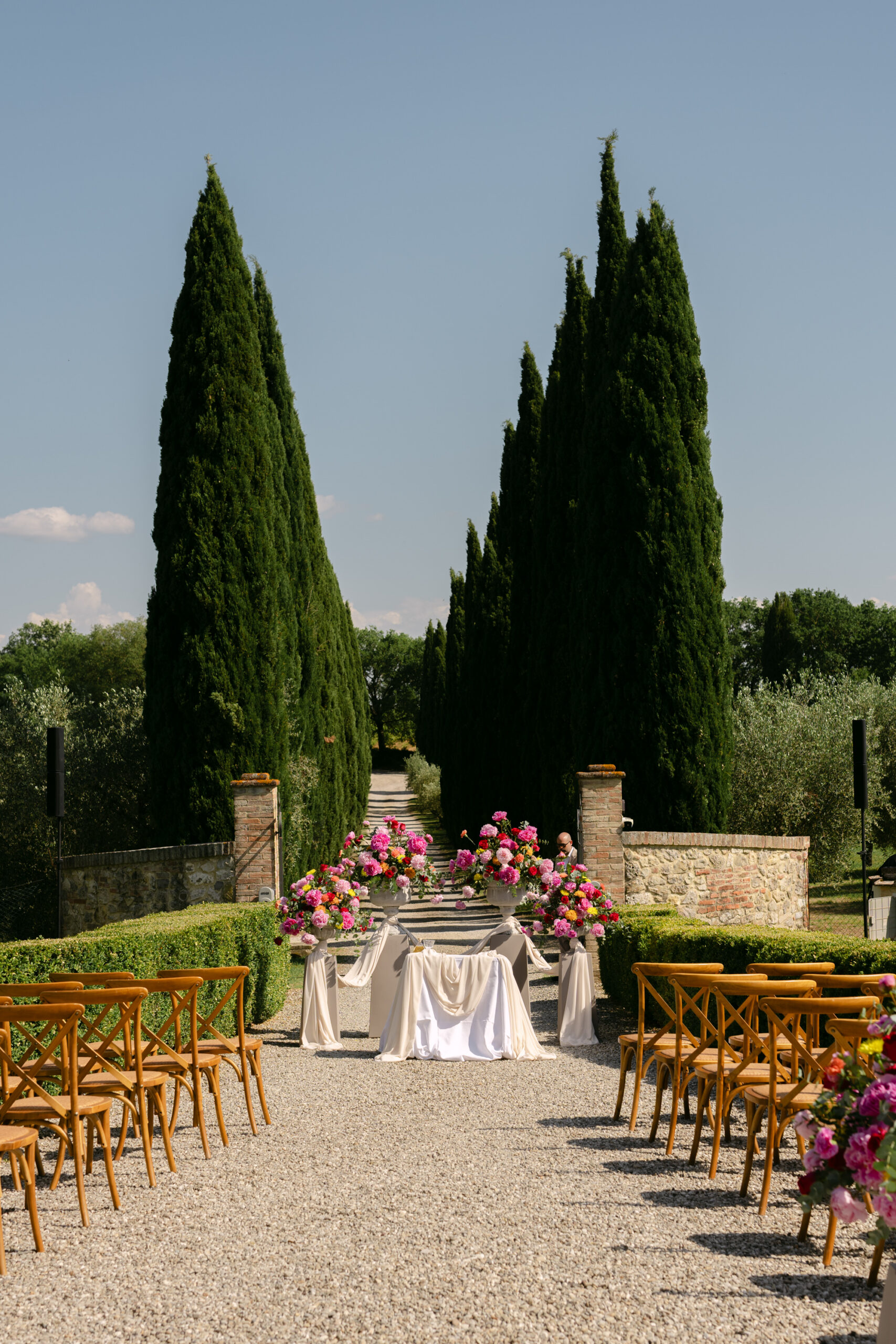 Cypress trees and bright pink wedding florals on stone pillars at the ceremony entrance, Val d Orcia Tuscany wedding