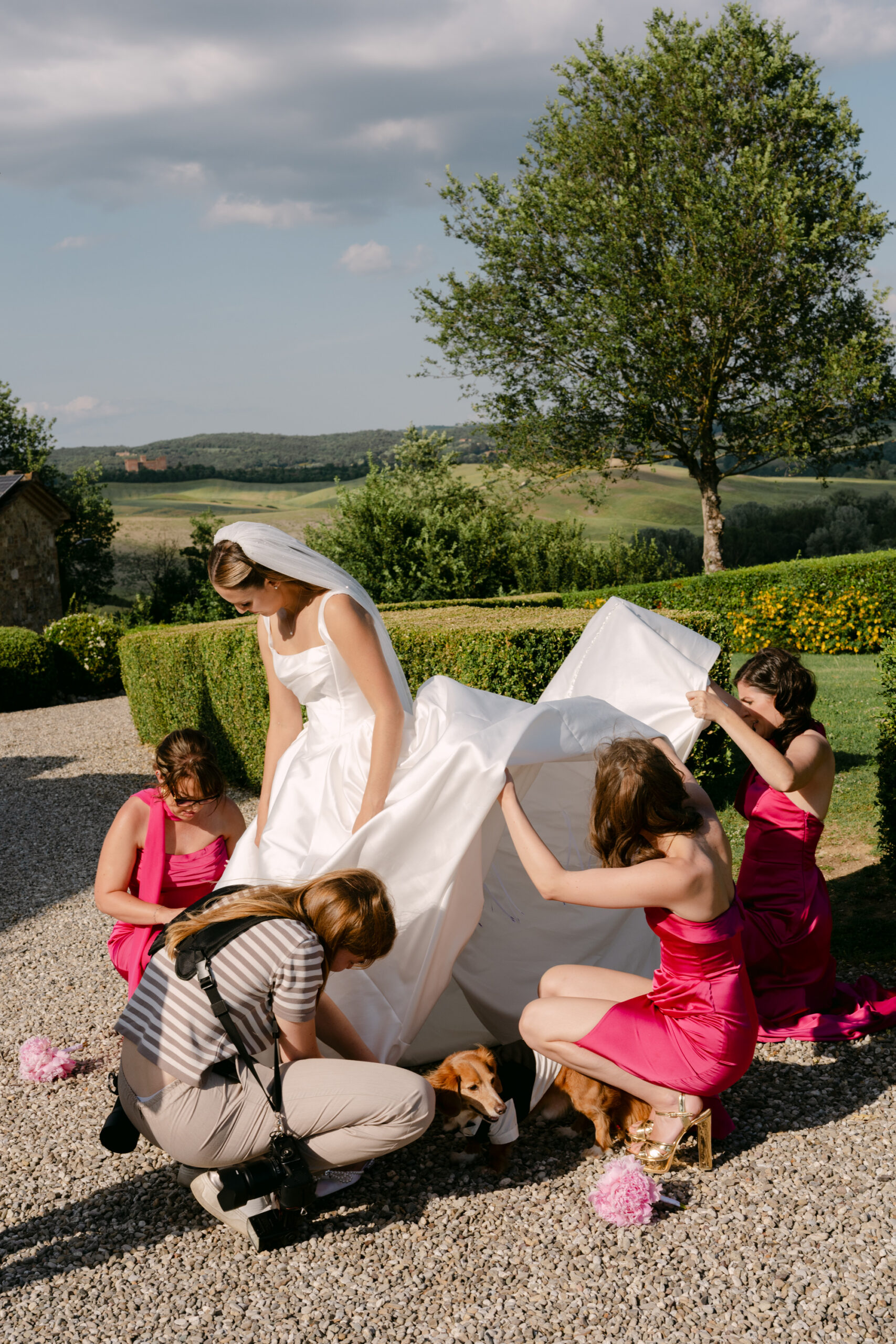 Bridesmaids in pink helping the bride with her gown before a destination wedding ceremony in Tuscany Italy