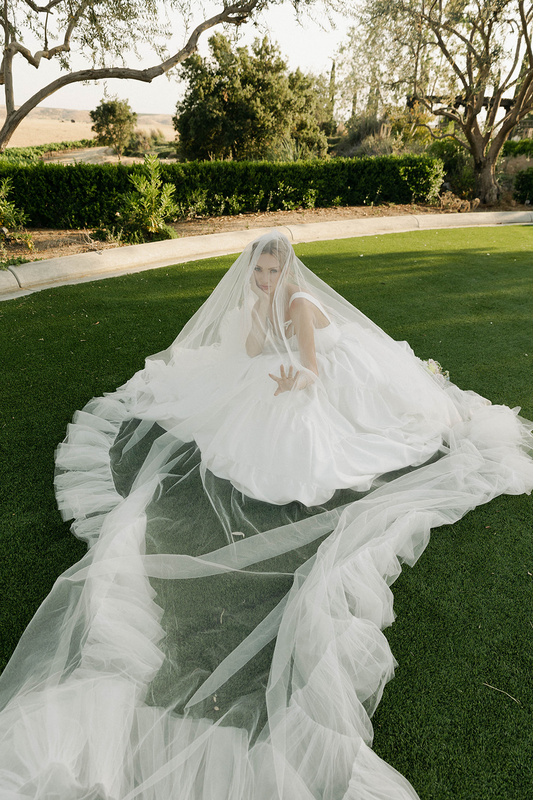Bride seated with her veil spread across the lawn