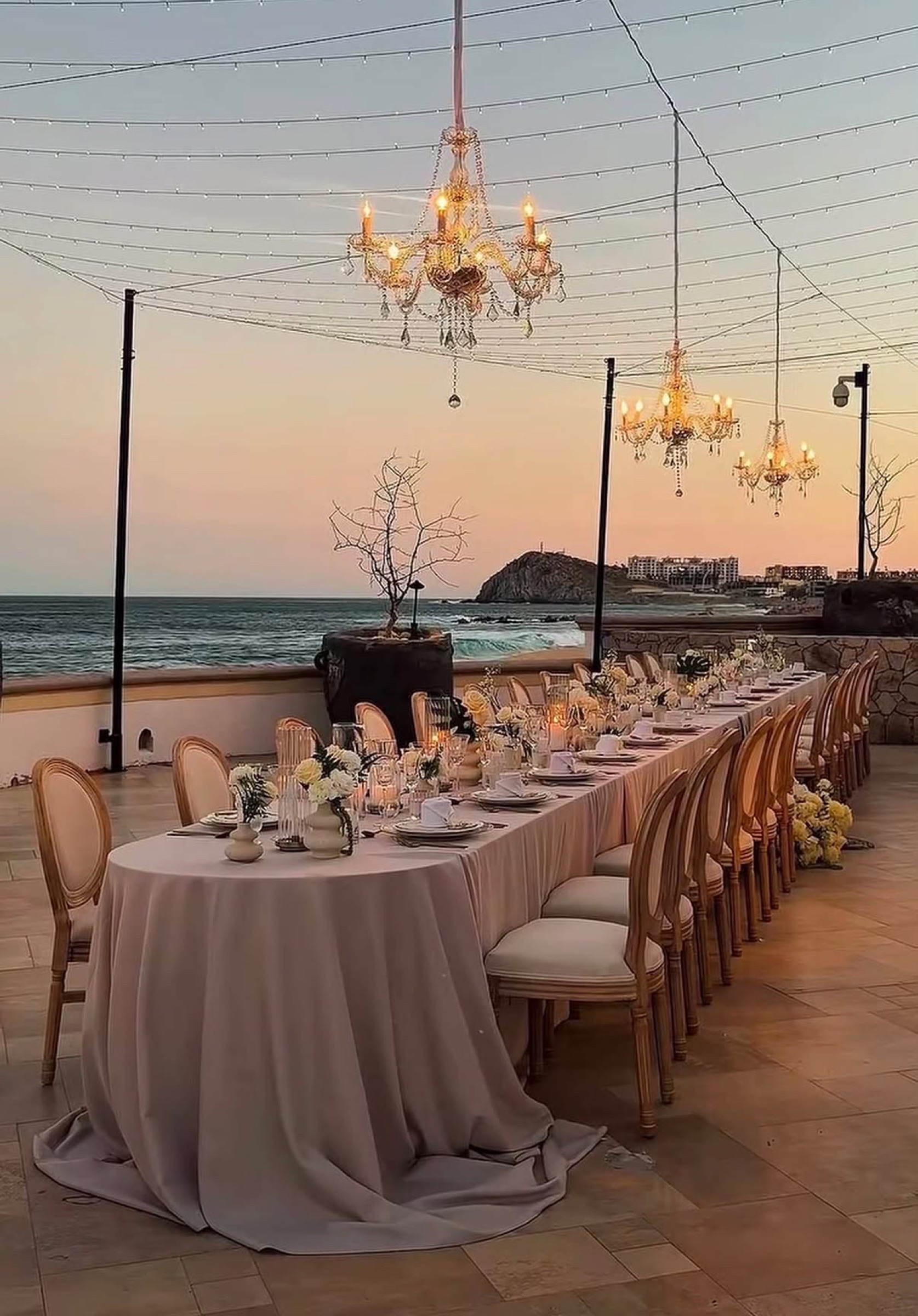 Oceanfront reception table beneath chandeliers at sunset