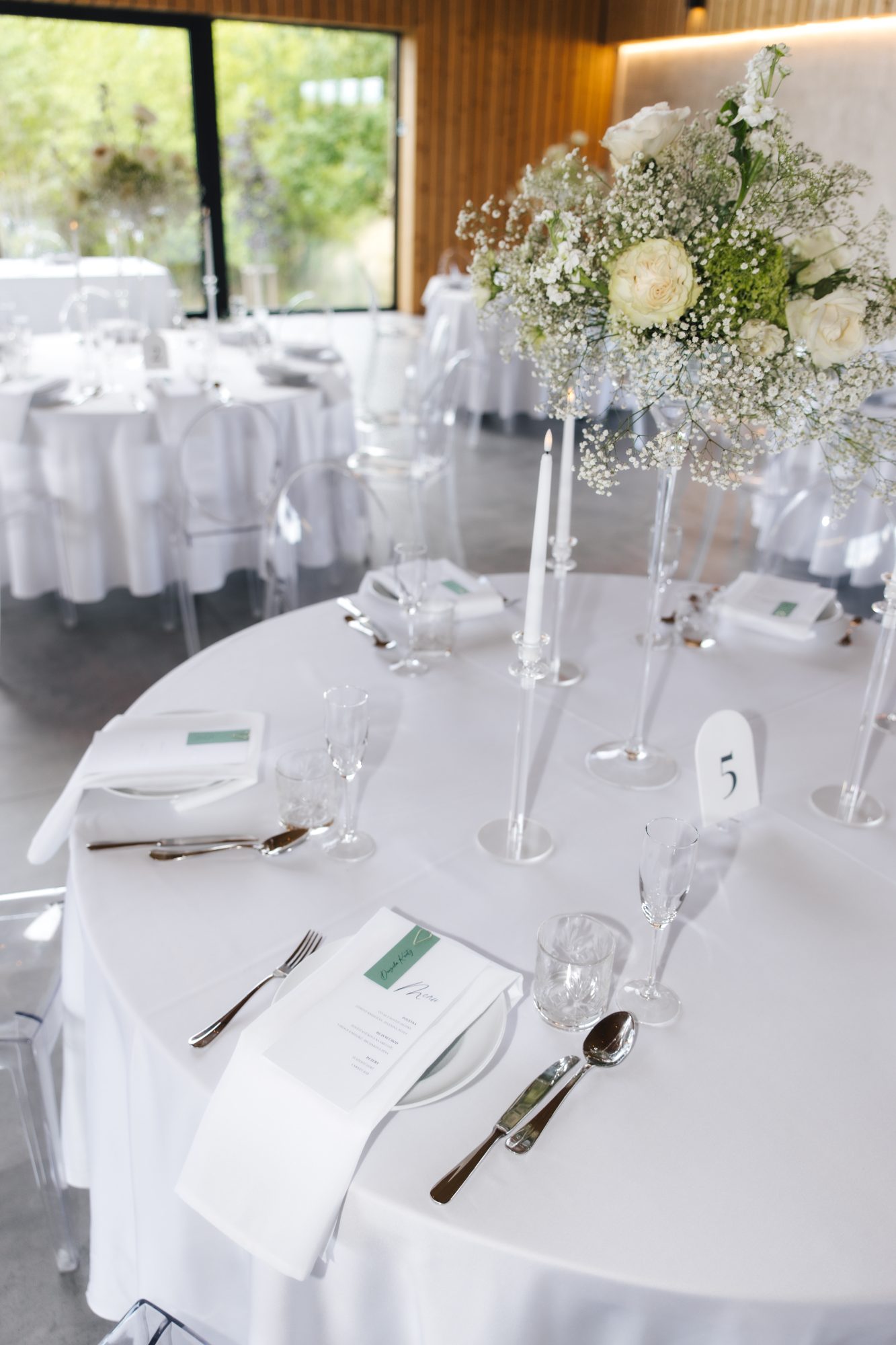 Round reception table with white linen, tall florals, and menu cards at a Czech wedding
